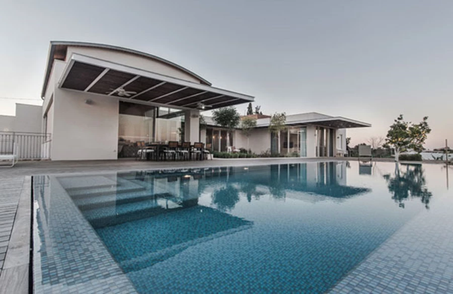 בריכת השחייה: בריכת גלישה מחופה אריחי פסיפס תכולים ממוקמת מול הנוף וכמו ממוקמת בתוכו.