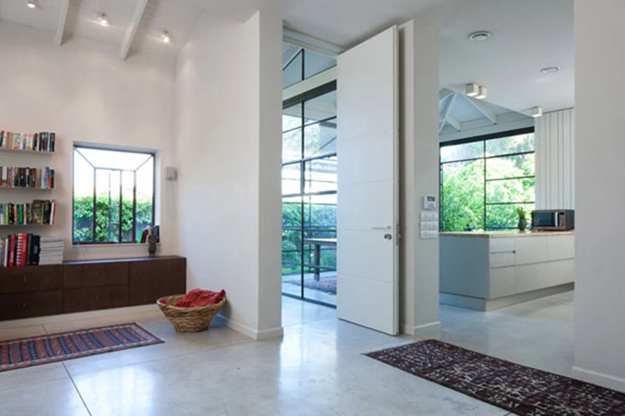 מבט אל הכניסה מתוך עומק החלל: דלת הכניסה מסמנת חלוקה לשני אזורים: אזור הסלון מימינה, ואזור מטבח-פינת אוכל מרווח משמאלה. עיצוב תאורה: גילה מוגרבי, גופי תאורה: 