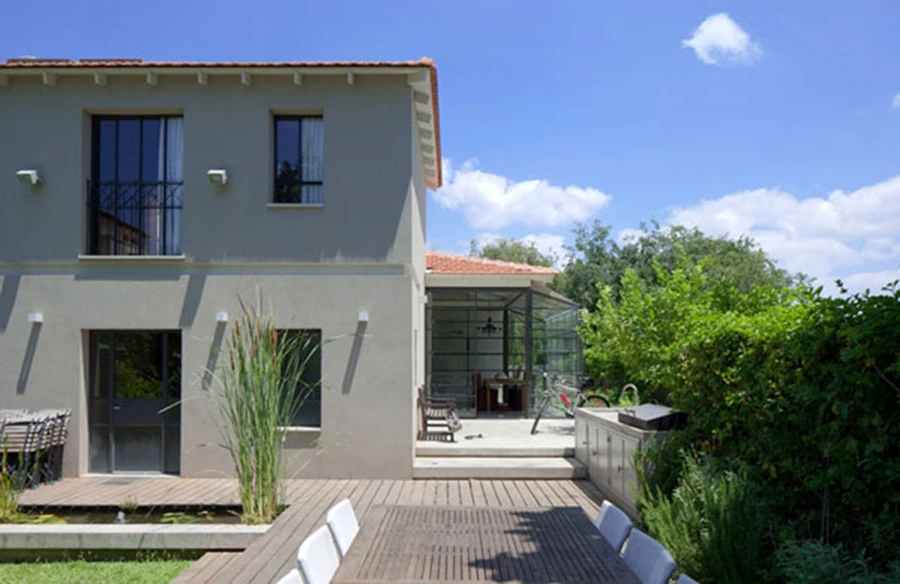 אזור האירוח שבגינה: מטבח חיצוני מאובזר בכל הפונקציות ולצדו ערוגת צמחי תבלין לשימוש מידי, פינת אוכל המייצרת ציר ישר עם פינת האוכל הפנימית כמענה לאופציות אירוח מגוונות, צמחייה ירוקה ובריכת נוי ביולוגית.