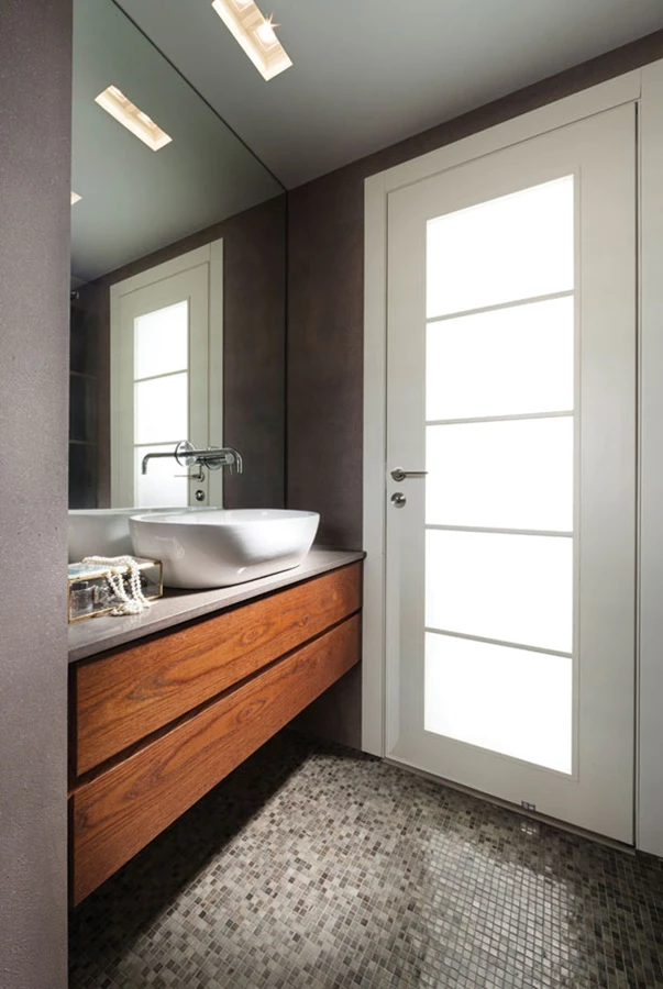 חדר הרחצה המופרד מהחדר באמצעות דלת אוורירית משולבת זכוכית. ריצוף פסיפס ויחידת אחסון מרחפת עם כיור אובאלי בהנחה עליונה. ריצוף פסיפס: