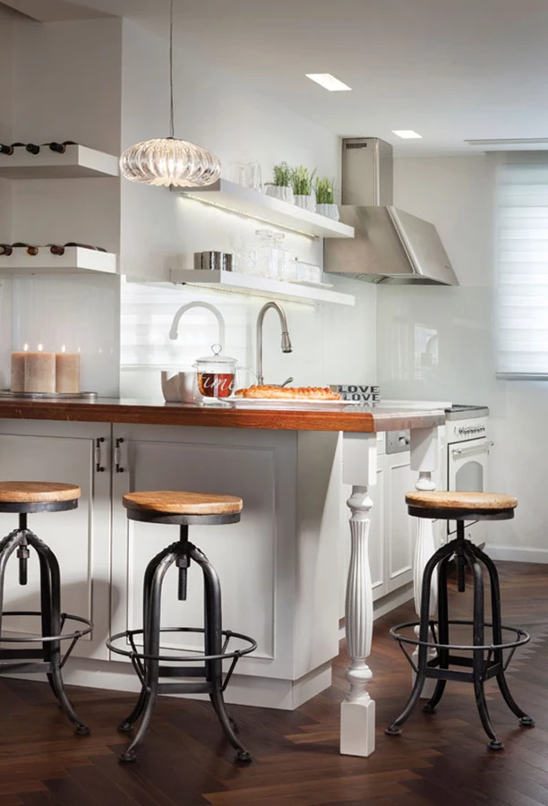 דלפק האכילה הפינתי שבקדמת המטבח: משטח עץ המתכתב עם פרקט העץ, רגל פיסולית בסגנון אנגלי-קישוטי, ושרפרפים עם בסיס ברזל היוצקים ממד צעיר. מעל הדלפק: מדפים לבקבוקי יין עם תאורה תחתית מתקבלים בשעות החשיכה כמקור אור חינני.