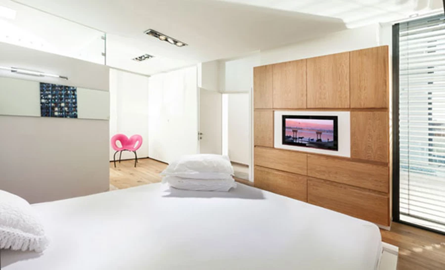 יחידת ההורים: מחיצת זכוכית חוצצת בין אזורי השינה, הרחצה והאחסון. ריצוף פרקט, חזיתות ארון מעץ בהן משתלב מסך הטלוויזיה ופתח יציאה אל החוץ.