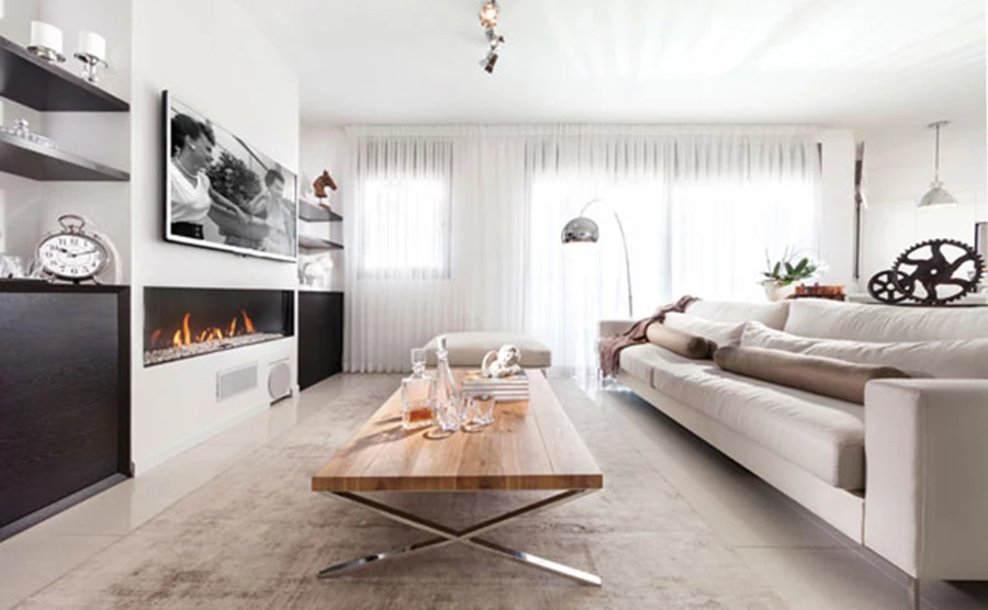 אזור הסלון שבחלל הפתוח:  מערך קיר שבמרכזו משתלב קמין ומשני עבריו גומחות המכילות מדפים ויחידות אחסון שעוצבו כקאסטם מייד מעץ אלון בגוונים שונים עם חיתוך גרונג. קמין: כרמל חימום, נגרות: נגריית דפני.