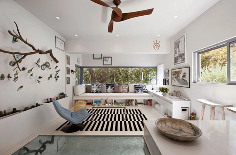 הסלון החולק מרחב משותף עם המטבח ונהנה מנוף ירוק של צמרות העצים. מבנה פינתי של ספה ויחידת אחסון שעוצבו ייעודית, שולחן קפה על גלגלים, כורסה משנות החמישים שנמצאה בשיטוטים, ויחידות בנויות שבתוכן משתלבות אדניות עם קקטוסים. להשלמת אפקט הצמיחה הירוק: קומפוזיציה מקורית המשלבת גזע עץ פיסולי ממנו משתלשלים חוטי דיג עם דליים קטנטנים וקקטוסים בתוכם. העיטור הנראה על קורה עליונה הוא לוגו של קו התכשיטים שמעצבת לורן.