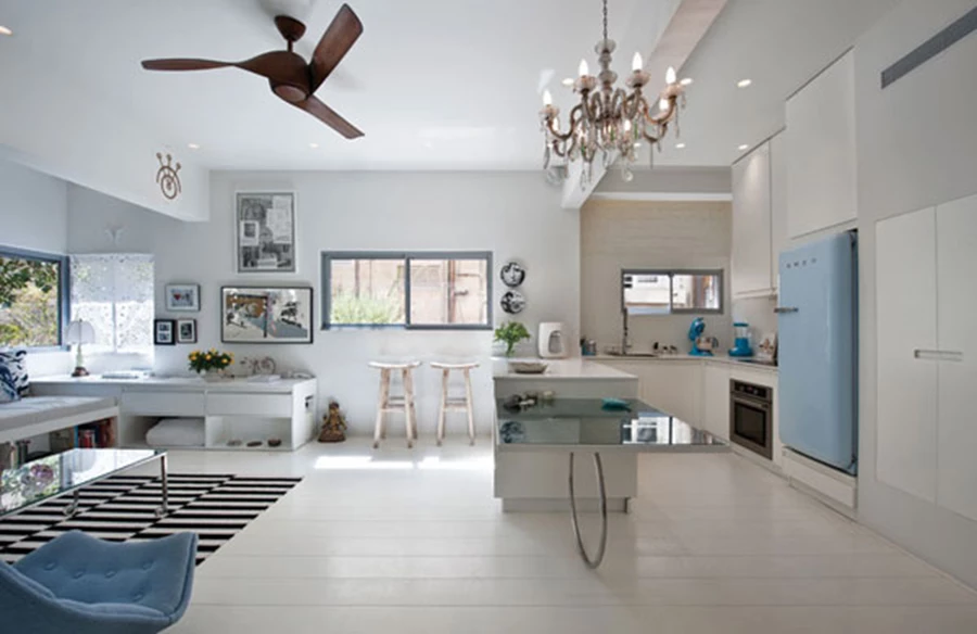 פרישת פונקציות מרווחת באזור הציבורי: מימין המטבח ומשמאל הסלון. בעומק המטבח נראה קיר לבני סיליקט שנחשפו במהלך השיפוץ, מקרר בגון תכלת בטעם של פעם