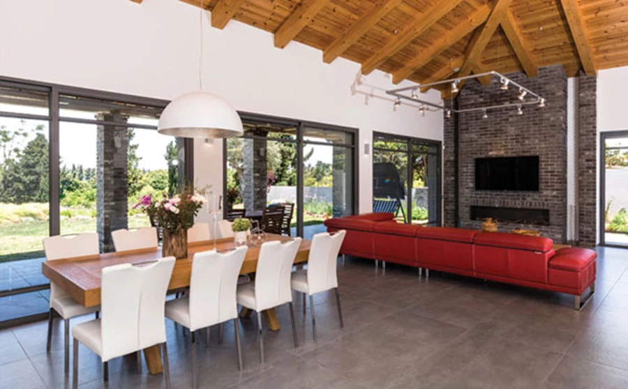 מערך ויטרינות מייצר חזית שקופה החושפת את נוף הגן. על קיר הלבנים מותקן מסך הטלוויזיה ובתוכו משתלב קמין אינטגראלי. ספה אדומה מייצגת את הגון האהוב על בני הבית ושולחנות הקפה והאוכל עשויים עץ אלון.