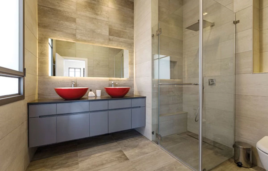 עיצוב מוקפד ומפנק בחלל הרחצה של יחידת הורים: מקלחון מרווח, וכיורים אדומים בהנחה עליונה על יחידת כיור אפורה ומרחפת. חיפויים ואביזרים סניטאריים: