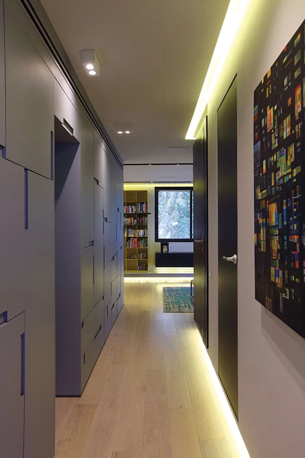 מבט אל עבר חלל המגורים מעומק המעבר שקירותיו מנוצלים למטרות אחסון. חזיתות בגון אפור בדיגום המדמה משחק טטריס, מונע תחושת מסה ומייצר עניין ויזואלי.