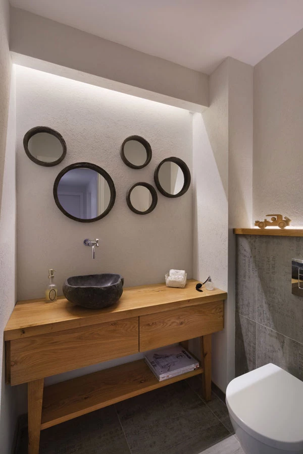 שירותי האורחים כנקודת חן: יחידה עשויה עץ אלון, כיור עשוי בזלת במופעה הטבעי וקומפוזיציה של מראות עגולות על הקיר.