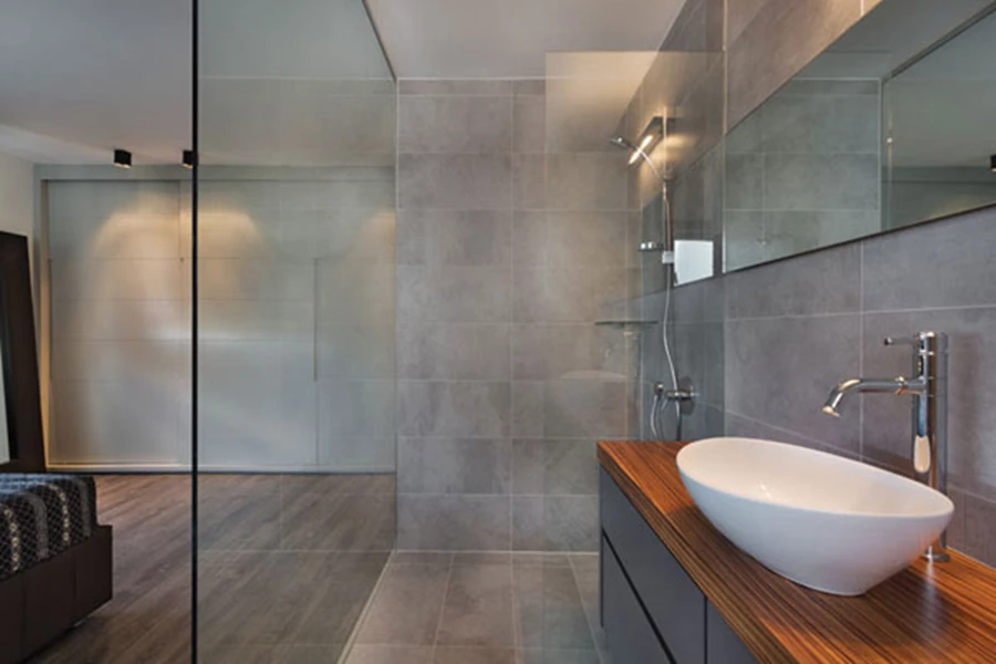 אזור הרחצה: ריצוף וחיפוי באריחי שיש אפורים המדמים בטון, ויחידת כיור בעבודת נגרות עם משטח זוברנו עליו מונח כיור גדול בעיצוב מסוגנן.