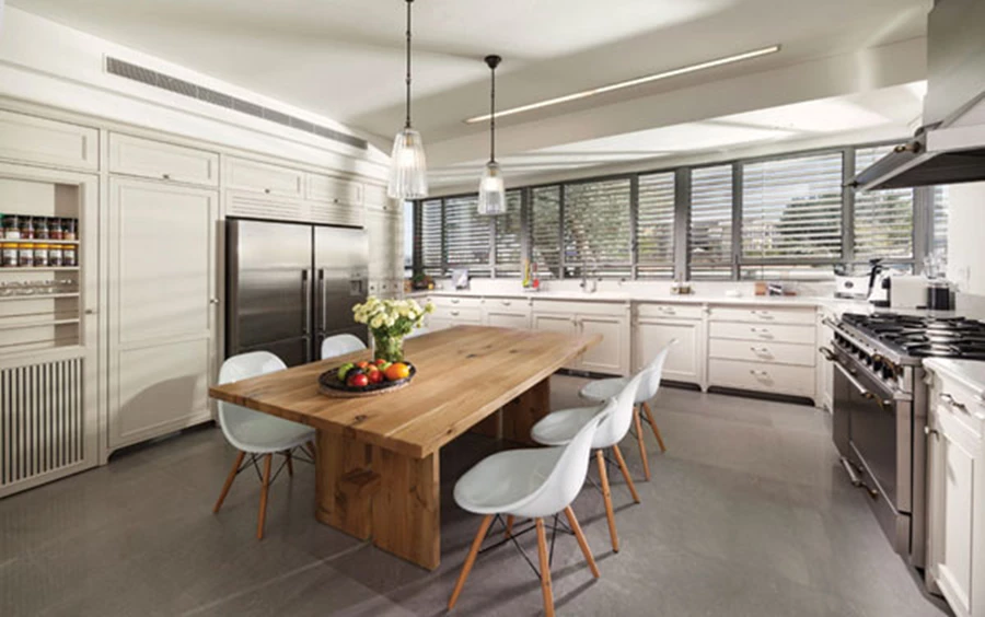 חמימות כפרית במטבח: חזיתות עץ בצביעה ידנית בגון שמנת עם פיגמנט אפרפר, ובמרכז החלל שולחן עץ גדול ומזמין. ביחידת הקיר: חזית