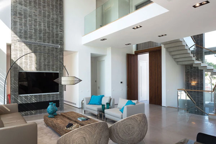 חלל המגורים, מבט מעומק החלל אל עבר דלת הכניסה: מימינה גרם מדרגות שמוביל לקומה העליונה, משמאלה מעבר למשרדה של אורלי, וממעל גשר-גלריה של הקומה העליונה חוצה את הגובה הרב ומקיים איתו קשרי עין ישירים. הגובה הכפול מגדיר את אזור הסלון.