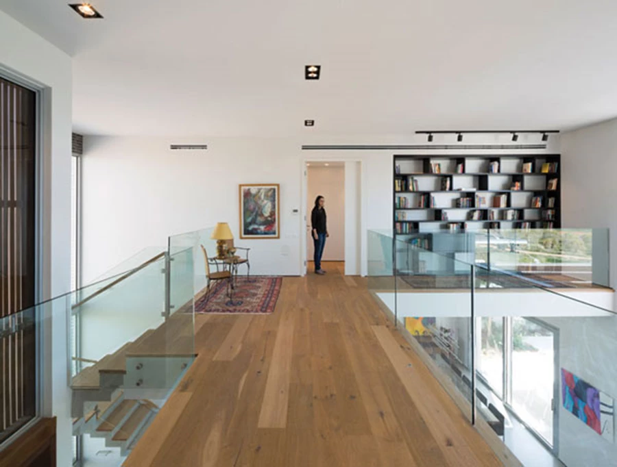 גשר הגלריה שבקומה העליונה: רחב מאד, זורם בתצורת L, ומייצר מופע של אזור בפני עצמו ולא של מעבר בלבד. בתמונה נראית הכניסה ליחידת ההורים, שכמו כל פתחי החדרים תוכננו כגבוהים מהמקובל עם דלתות בגובה 2.80 מ