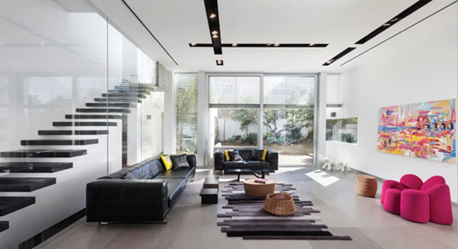 חלל המגורים: גבוה ואוורירי, ומקושר לגינה האחורית באמצעות ויטרינות גדולות.ריצוף באריחי שיש אפורים, קירות לבנים, וסטוקו מבריק בקיר גרם המדרגות, שצדו השני תחום במחיצת זכוכית. גופי תאורה שקועים בתעלות שחורות מייצרים דיגום גראפי בתקרה. תאורה: