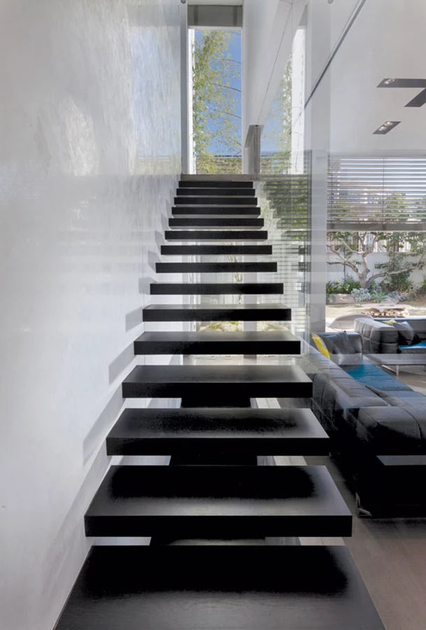 גרם המדרגות: קונסטרוקציית ברזל ומדרגות עץ כהות דרכן ניתן להציץ אל הגינה והפטיו המצויים מאחוריו. פודסט ביציקת בטון הנדסית נדמה כקובייה מרחפת, ופסי תאורה בתחתית המדרגות משרטטים משחקי אור על קיר הסטוקו המבריק, תוך יצירת מראה של אלמנט תאורה פיסולי. מסגרות: ארז תליו.