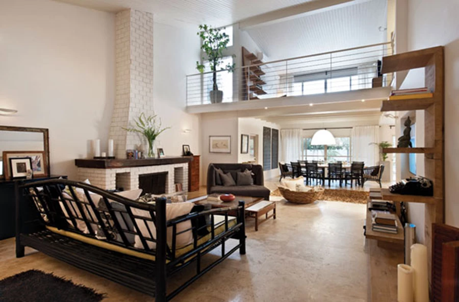 חלל המגורים והגלריה הצופה אליו ונצפית ממנו. הקמין והארובה כאלמנטים שנותרו כשהיו בבית הוותיק, ומשתלבים כבעלי משמעות נכונה גם במרחב המחודש. ריצוף באריחי אבן טרוורטין, קירות בגון שמנת, ספת במבוק בריפוד פשתן, ומדפי עץ אלון המאכלסים ספרים ופריטי נוי מובחנים. ריצוף: