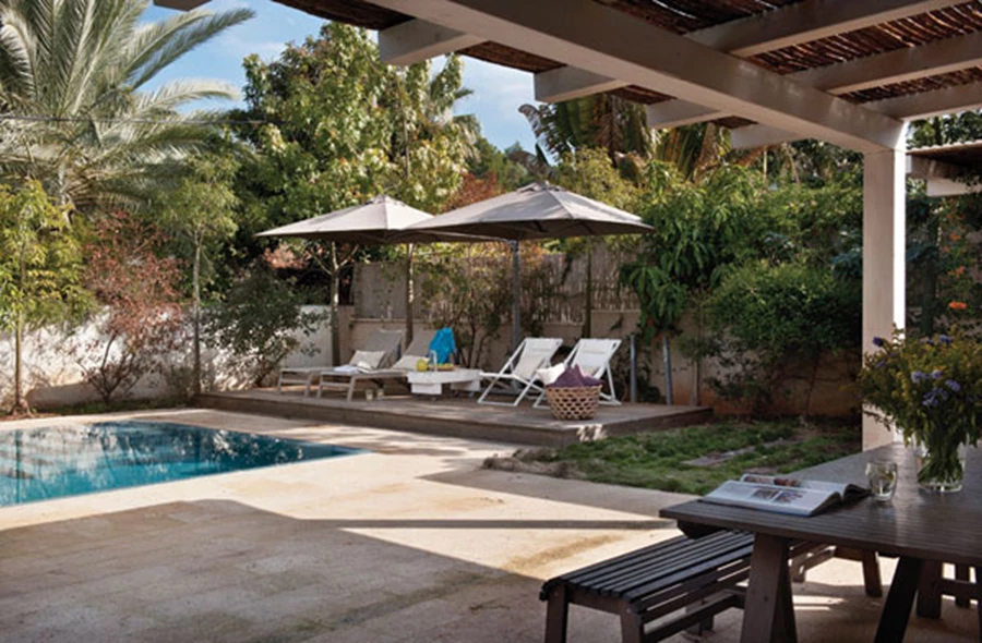 הגינה, ברוח הפשטות הטובה של עיצוב הפנים: גינון ארצישראלי נכון למקומו, ריצוף באבני כורכר טבעיות עם שילוב עץ אורן ואדני רכבת מפירוק, ובריכת גלישה כפינוק.