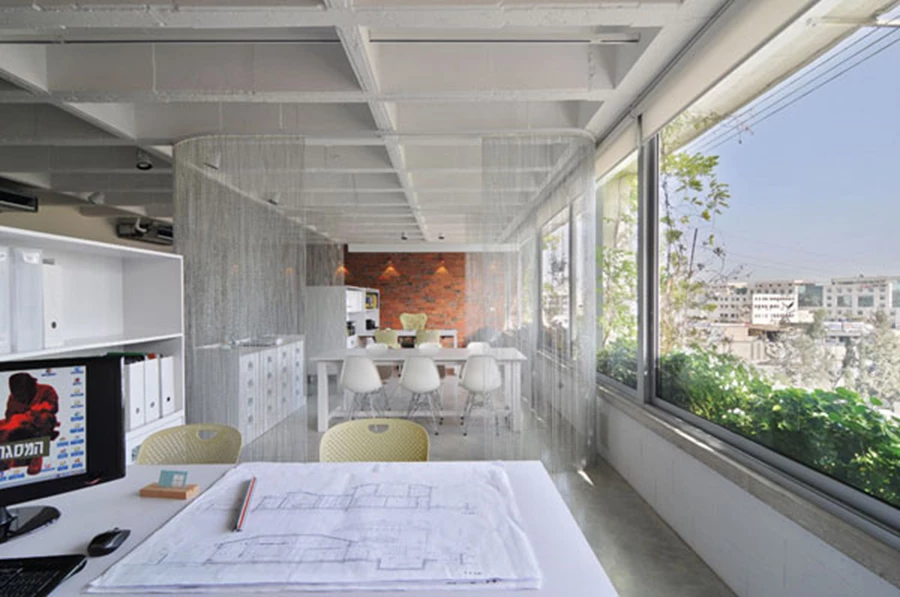 פתרון לפתחים דרומיים גדולים: העתקתם מעט פנימה לתוך החלל כשהקירוי בקו המעטפת מעניק להם הצללה נדרשת, ווילונות מסנני קרינה. השטח החיצוני שנותר אגב כך מנוצל כערוגה עם מערכת השקיה אוטומטית העושה שימוש במי המזגן. מעל הערוגה: פרגולה עשויה כבלים