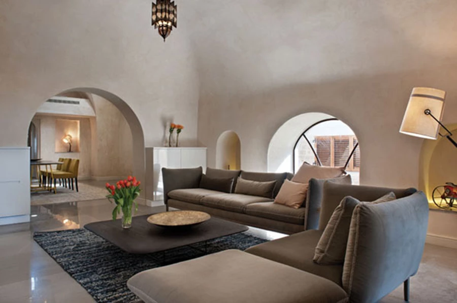 מבט מאזור הסלון הממוקם בחלל כיפתי אל עבר חלל פינת האוכל. פינת ישיבה עכשווית-נינוחה, שטיח למראה חמים, גופי תאורה כאלמנטים פיסוליים, ופריטי נוי מסוגננים. ריהוט (כל חללי הבית): אריק בן שמחון, גופי תאורה דקורטיביים: