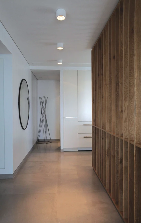 מבואת הכניסה: מחיצה מעוצבת כקורות עץ (אלון) אנכיות מגדירה הפרדה מהמטבח שמוקם בקדמת החלל: אלמנט המייצג שילוב של גריד צורני שנגזר מנוף המגדלים וחומר שמהדהד את פיסת הטבע שמציצה לצדו. | נגרות: אלון הרצוג.