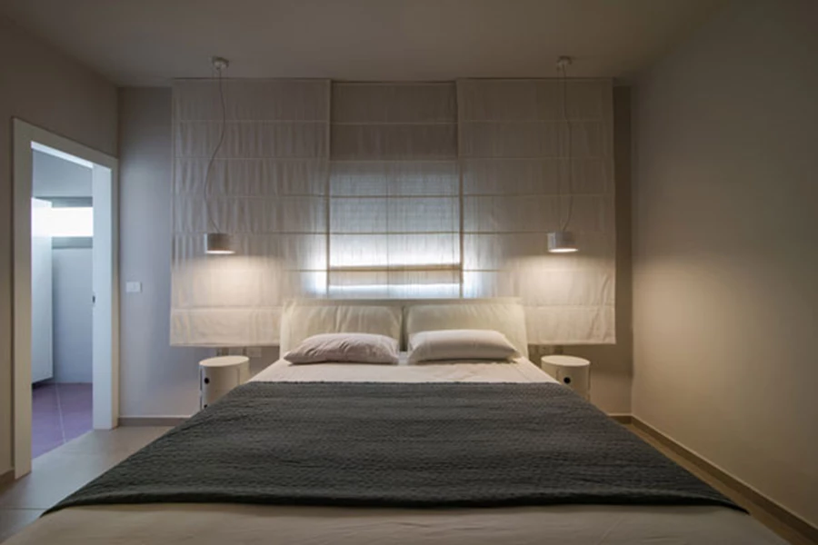 שני גופי תאורה יורדים לכיוון שידות מעוגלות, ויוצרים מסגרת אינטימית למיטה