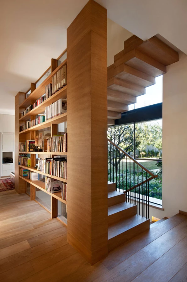 ספרייה התוחמת את גרם המדרגות מסננת את האור החודר מבעד שקיפות הזכוכית.