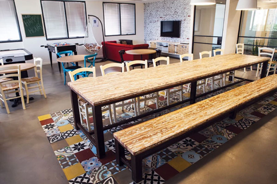 לריצוף המרחב משמש בטון מוחלק, ובחלק משטחו משתלבים אריחים מצוירים תוך יצירת שטיח צבעוני המהווה רקע לשולחן וספסל