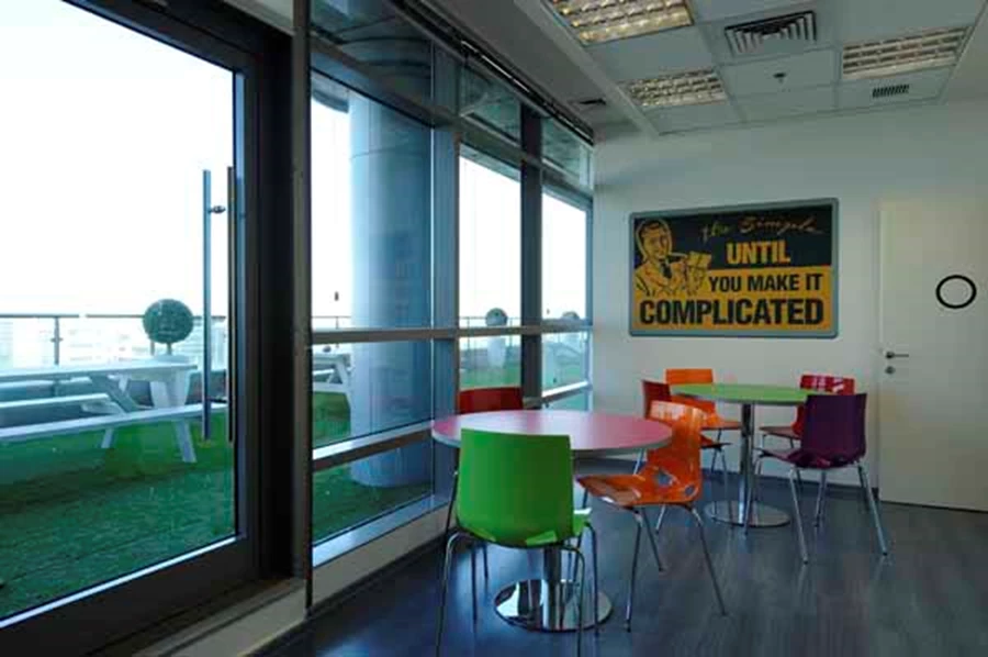 חלל המטבח ופינת האוכל: פריטי ריהוט צבעוניים כמו בכל חללי המשרדים, ומבט אל המרפסת.