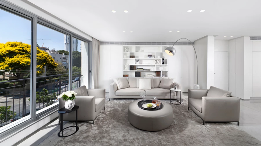 מבט מעומק הסלון אל עבר הכניסה: חלל פתוח ומזמין בו מתקיים שיח הרמוני בין ניקיון עכשווי לחמימות ביתית.