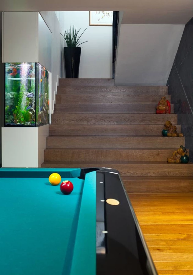 מדרגות העץ המובילות אל המרתף נמתחות לכל הרוחב, כסוג של אמפיתיאטרון המשקיף אל החלל. במקום מעקה משמש אקווריום של מים מלוחים שהיותו מואר משמש גם כגוף תאורה מקורי, נוסך תחושת מרחב ומעשיר את החלל בנוף פנימי מיוחד.