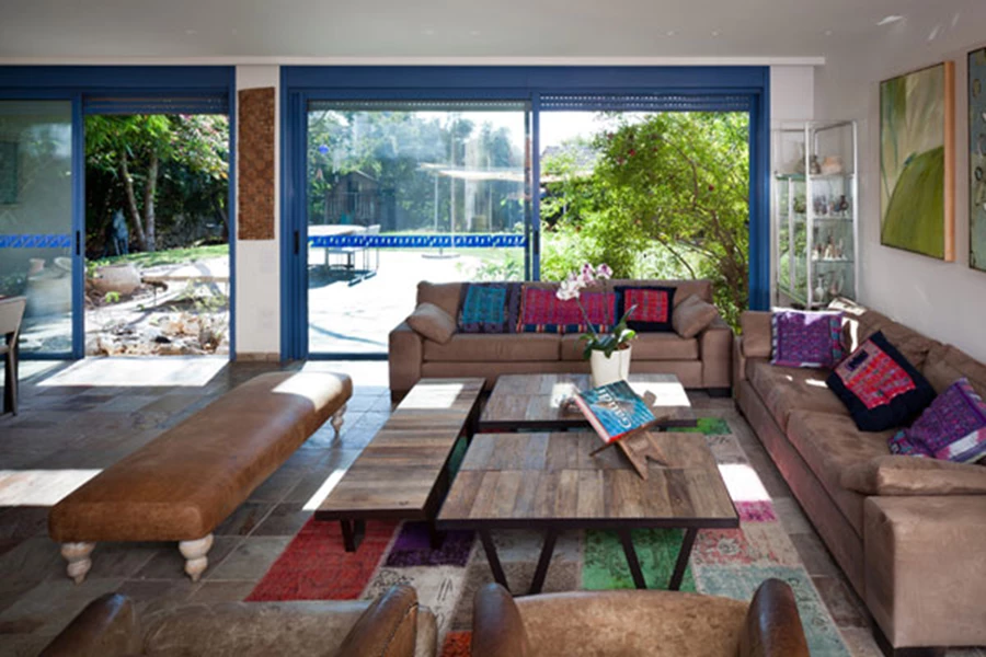 חלל המגורים הפונה אל הגינה :פתחים כחולים עוטפים חלל צבעוני וחמים בו מודגשת אמירה אישית. שולחנות קפה: