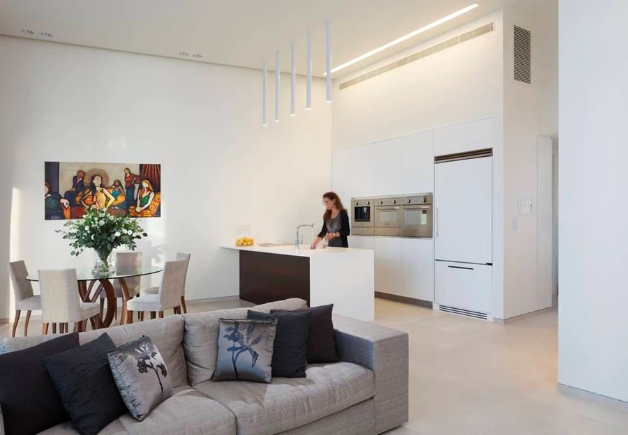 המטבח שבקדמת החלל הציבורי צופה אל הנוף. לבן כגון שולט, יחידת קיר עם חזיתות בגימור אפוקסי ויחידת אי עם משטח קוריאן מלווה בגופי תאורה מסוגננים המשתלשלים מעליה. מטבח: