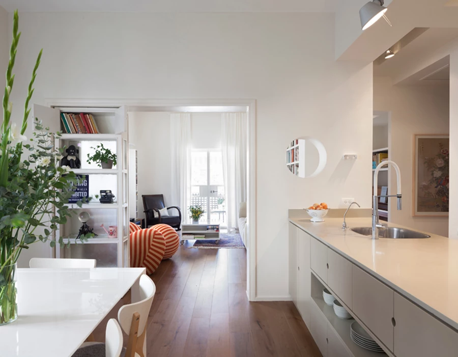 מבט מחדר האוכל לסלון: אחת מכנפי דלת החיבור בין שני החללים משמשת כוויטרינה ומייצגת אלמנט טיפוסי לתקופה בה נבנתה הדירה. מימין נראית יחידת האי של המטבח.