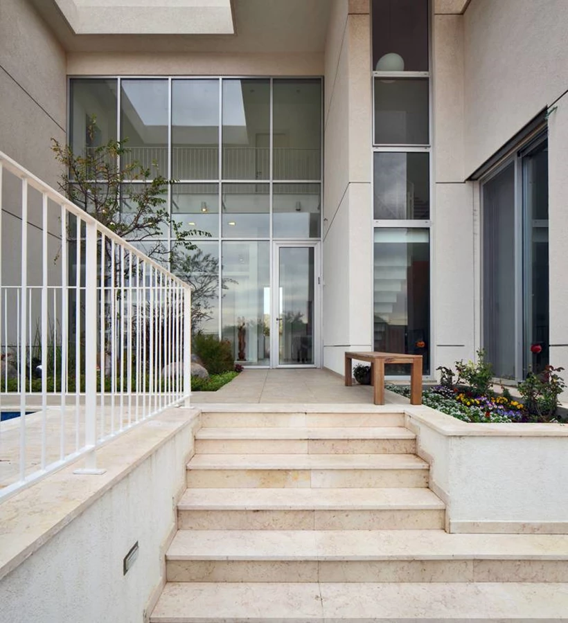 הכניסה לבית: כתהליך שכבות מדורג המתחיל בשער החצר, עולה מספר מדרגות, מגיע למבואה חיצונית מוגדרת, חולף על פני חלקה מגוננת ומגיע אל חזית שקופה מזמינה שדרכה נגלים הספרייה וגשר הגלריה של הקומה העליונה.