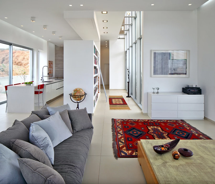 מבט מעומק הסלון: אלמנט הספרייה מהווה הפרדה בין המבואה לבין המטבח המוצנע מאחוריו. תכנונו במנותק מהתקרה וגובה כפול שנשמר באזור המבואה מייצרים תחושת פתיחות וזרימה בין האזורים.