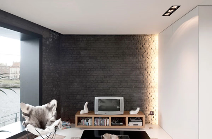 במרווח שבין ארון האחסון לקיר המעטפת מותקנת תאורה נסתרת המדגישה את קו התפר שבין הישן והחדש.