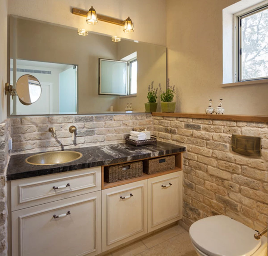 חדר הרחצה של יחידת ההורים: עבודת נגרות וחיפוי קירות בלבני פירוק עם שילוב אריחי גרניט פורצלן תואמים במקלחון. אביזרים סניטריים: 