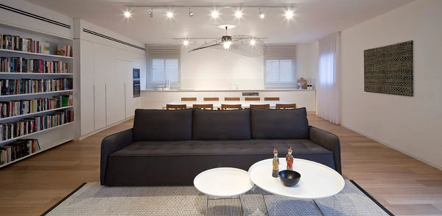 מבט מאזור הסלון אל עומק החלל: מרחב נקי, בהיר ואוורירי, שהפונקציות השונות סדורות בו ברצף. אזור הסלון בחלקו הקדמי, מאחוריו פינת האוכל, ובעומקו המטבח.ריצוף פרקט: