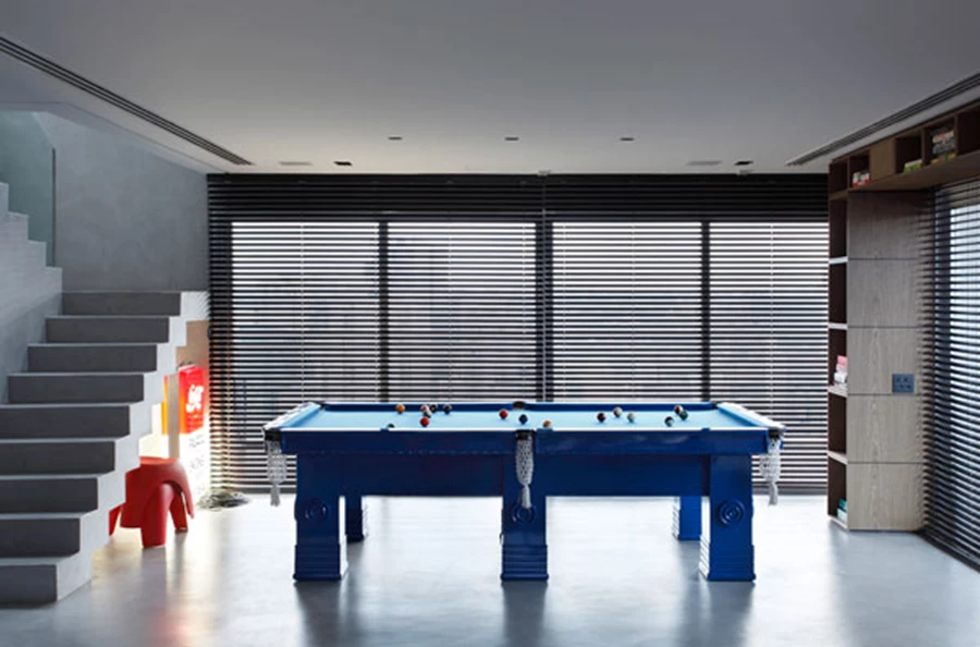 שולחן הביליארד שנצבע בכחול, והמדרגות המובילות לקומה העליונה, נטולות מעקה ומחופות במלט במרקם חלודה המשמש לחיפוי כלל קירות הדירה. למטה