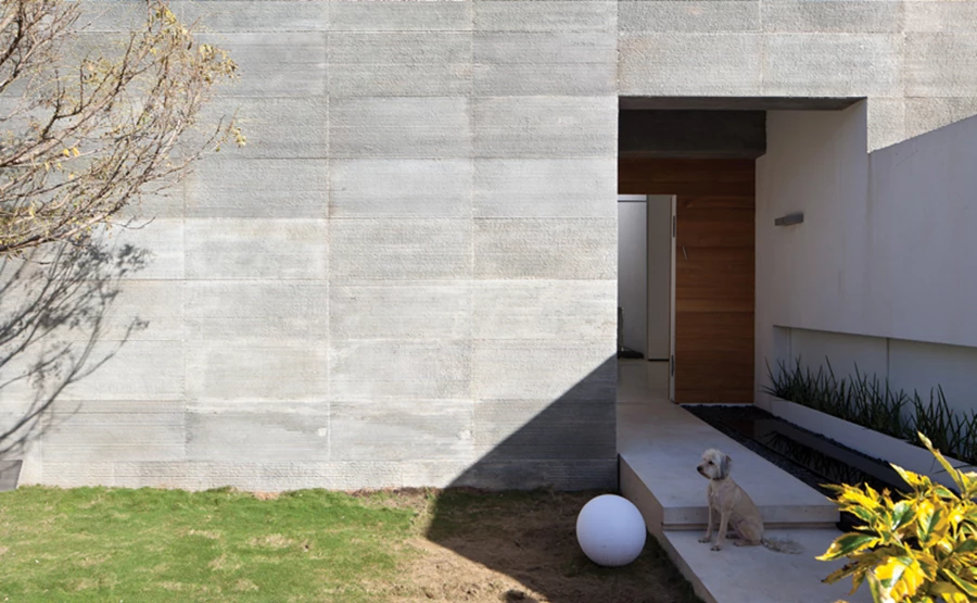 החזית הקדמית - אטומה לחלוטין ומחופה אבן אפורה בעיבוד מסורק. בריכת שיקוף זורמת במקביל לשביל המעבר אל הבית, תחומה בחיפוי חלוקי נחל וצמחי שבטבטים. הקיר מימינה מפריד בינה לבין החניה ופתח אופקי שנפער בו הינו חלק משפת התכנון המקיפה את כל המרחב.