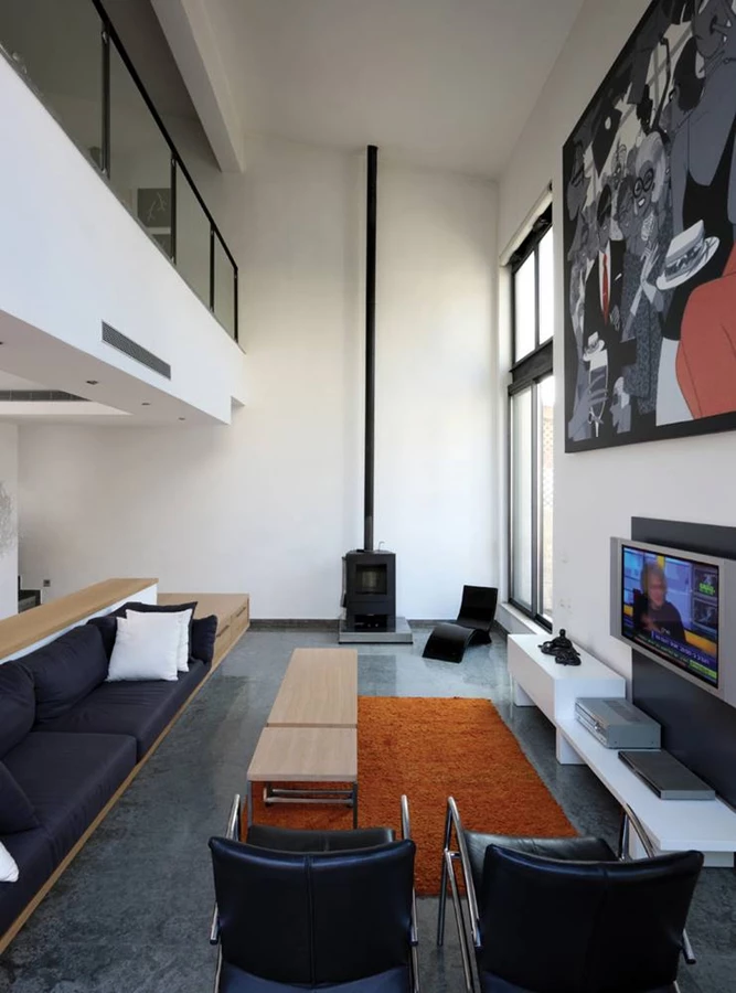 חלל הסלון הממוקם בקומה התחתונה: חלל גבוה המאופיין בתחושת פתיחות, כשהוא נצפה מהקומה שמעליו ופתחים גדולים קושרים אותו ישירות אל החצר. שפת עיצוב אנינה ומינימליסטית הנשענת על צמצום “כמותי”, משמרת את ממדי הפתיחות והאווריריות. ארובת אח הברזל היצוק “מטפסת” לכל גובה הבית ומשרתת גם את הקומות האחרות. עבודת אמנות מרשימה בממדיה, המגלמת תוכן אישי השזור בשפת הבית, מלווה את האזורים הציבוריים ובתוך כך מהווה סוג של אלמנט המדגיש את החיבור ביניהם.