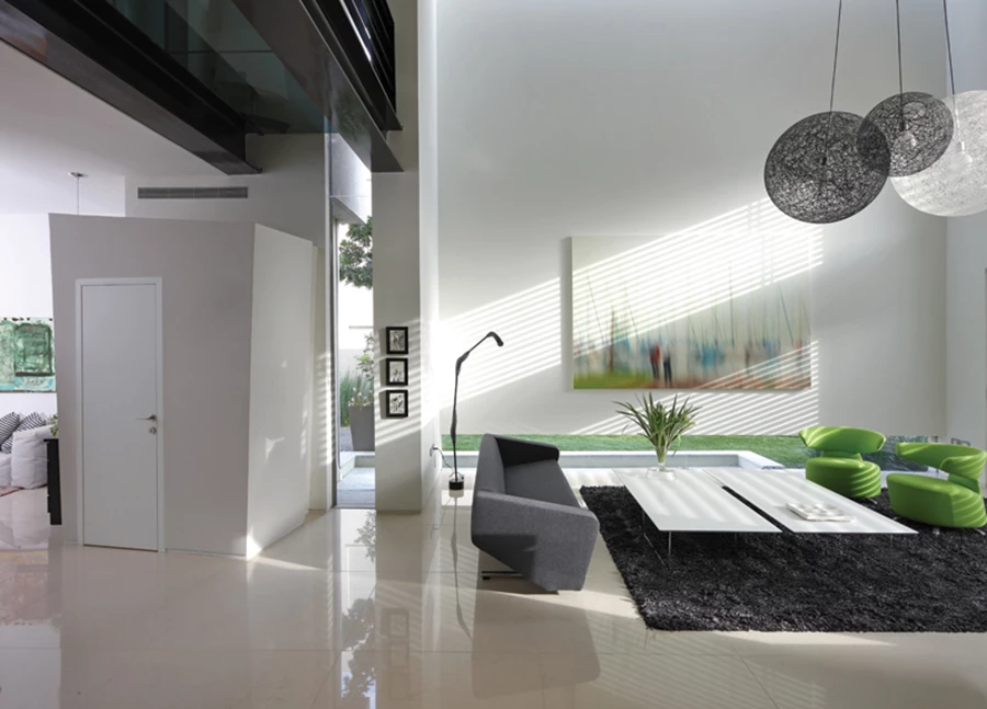 חלל הסלון, שהינו היחיד שגובהו כפול, והגשר החוצה מעל. פתחים בגיאומטריות משתנות מייצרים איזון בין אינטימיות ופתיחות: פתח סרט בחלקו התחתון של קיר ופתח סקיילייט מעל חלקו העליון משווים לו מראה מרחף ומנותק, ופתח אופקי המנצל את ממד גובהו של החלל משולב מעל פתח יציאה לגינה האחורית. סגנון העיצוב מודרני, ופלטת הצבעים מתבססת על גווני לבן, אפור ושחור עם שילובי צבעוניות עזה. ספה:”פיטרו”, כורסאות ירוקות:”טולמנ’ס”. גוף תאורה המשלב שלושה כדורים מעוצבים כמעשה מקלעת: “קרני תכלת-אלקבס”.