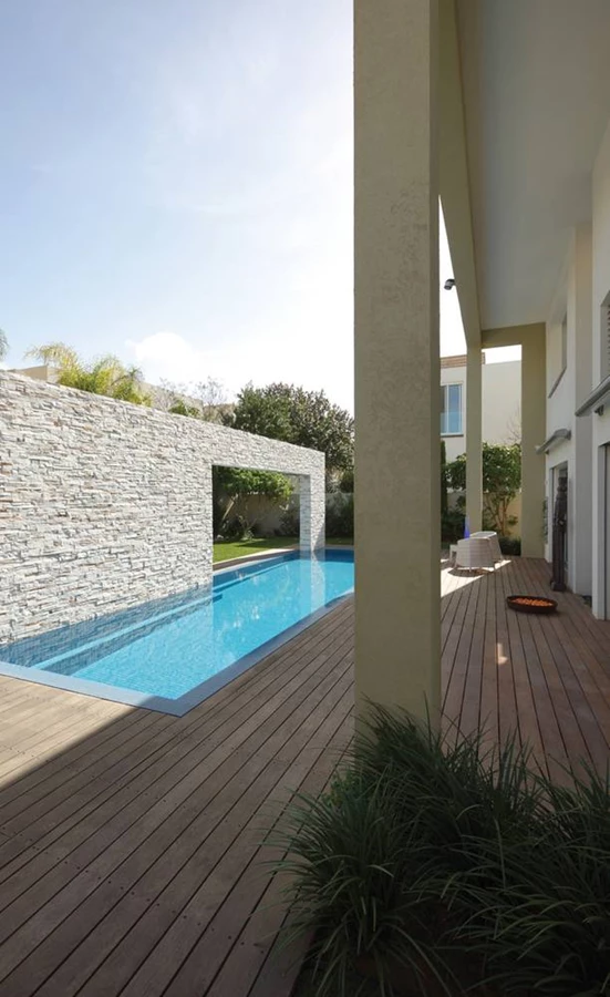 מבט מפינה של הדק אל עבר מבנה שער מחופה אבן תעשייתית שתוחם את אחת מצלעות הבריכה ותוכנן לשמש כמסתור ויזואלי מפני הבית הממוקם מאחור.