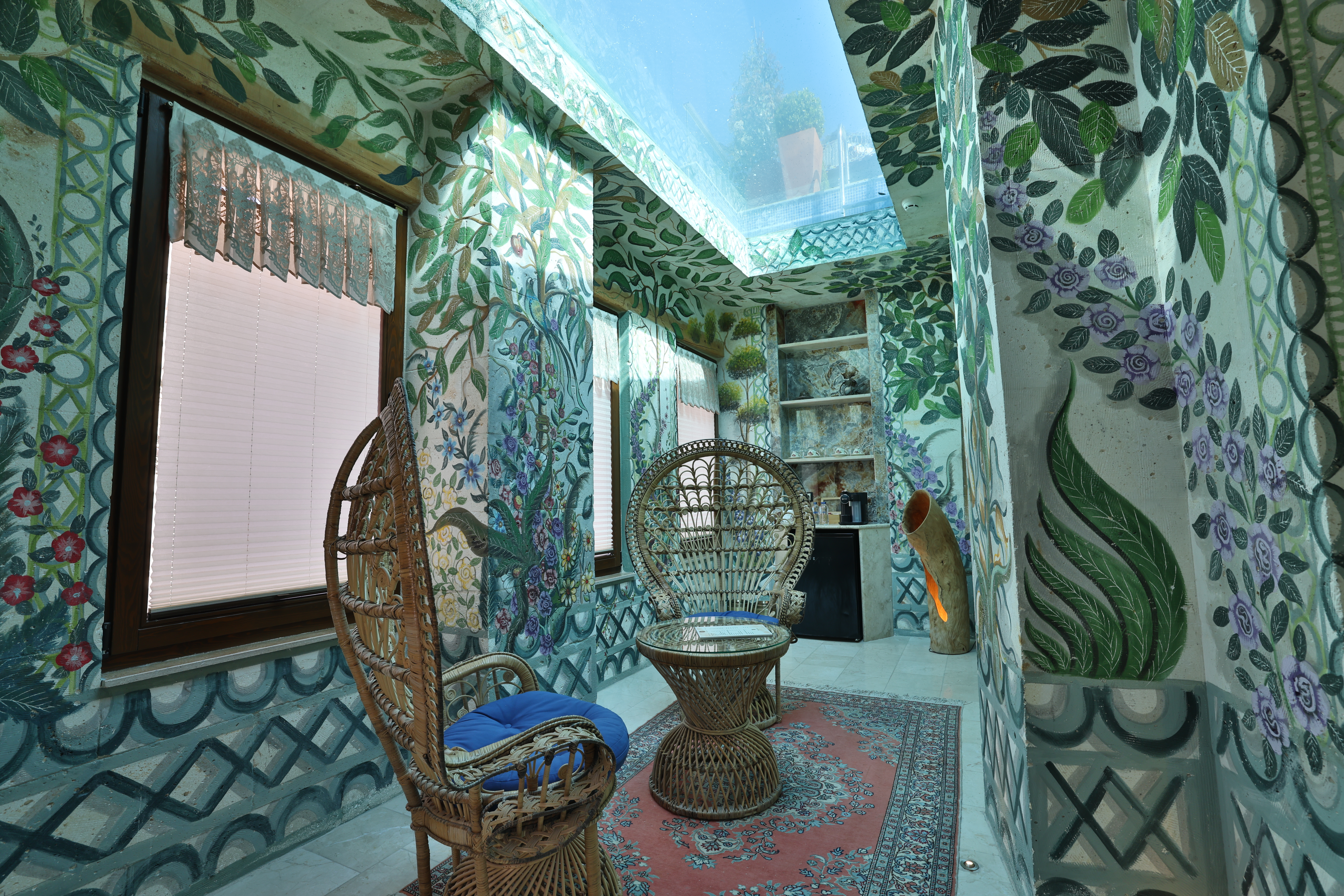 חדר שינה בוילה של Elika Cave Suites Cappadocia, עם תקרת אבן מקושתת, מיטה גדולה עם ראש מיטה מעוטר, נברשת ופינת ישיבה ליד החלון. © 2026 Hilton